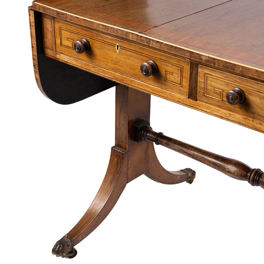 Close-up of an antique wooden writing desk with three drawers, decorative drawer pulls, a drop-leaf design, and a turned pedestal leg on a white background.