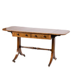 An antique wooden drop-leaf table with two drawers, turned legs, and brass casters, shown against a plain white background.