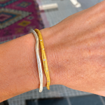 Two bracelets, one gold and one silver, on a wrist with a blurred background.