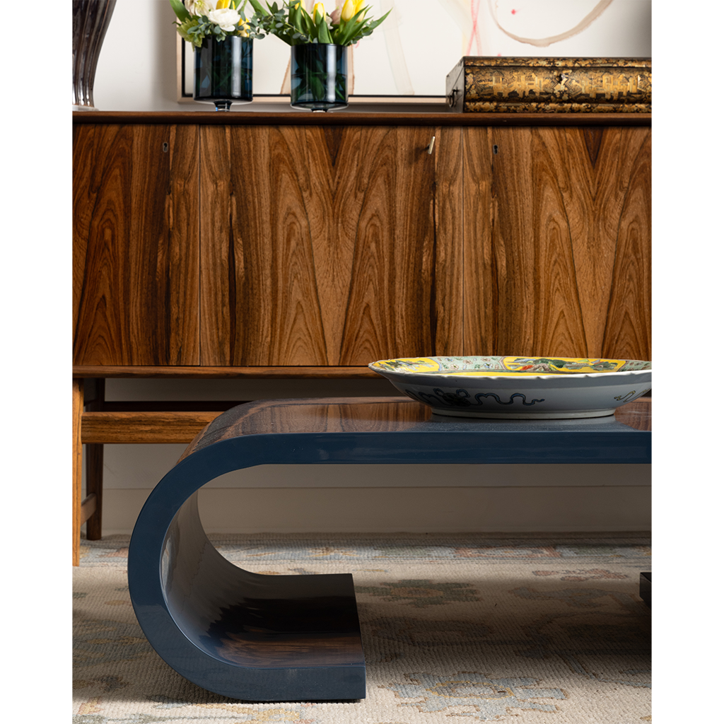 Modern blue coffee table in front of a wooden cabinet with decorative items.