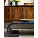 Modern blue coffee table in front of a wooden cabinet with decorative items.