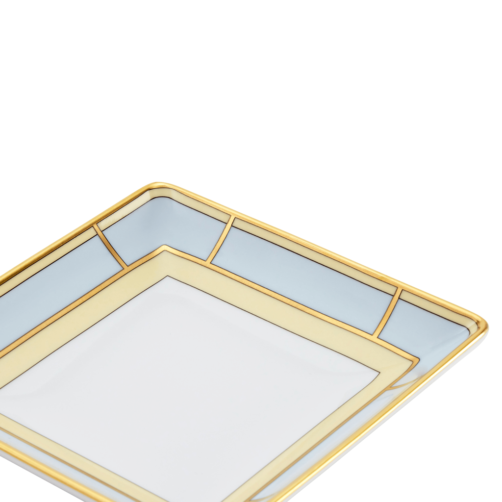 A light blue and yellow, square-shaped porcelain change tray with gold geometric patterns on the border.