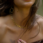 Close-up of a person wearing a gold necklace and earrings with a blurred background