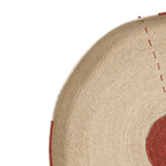 Close-up detail of a woven natural fiber product, showing a beige textured surface with red stitched accents and a partial red circular motif on a white background.