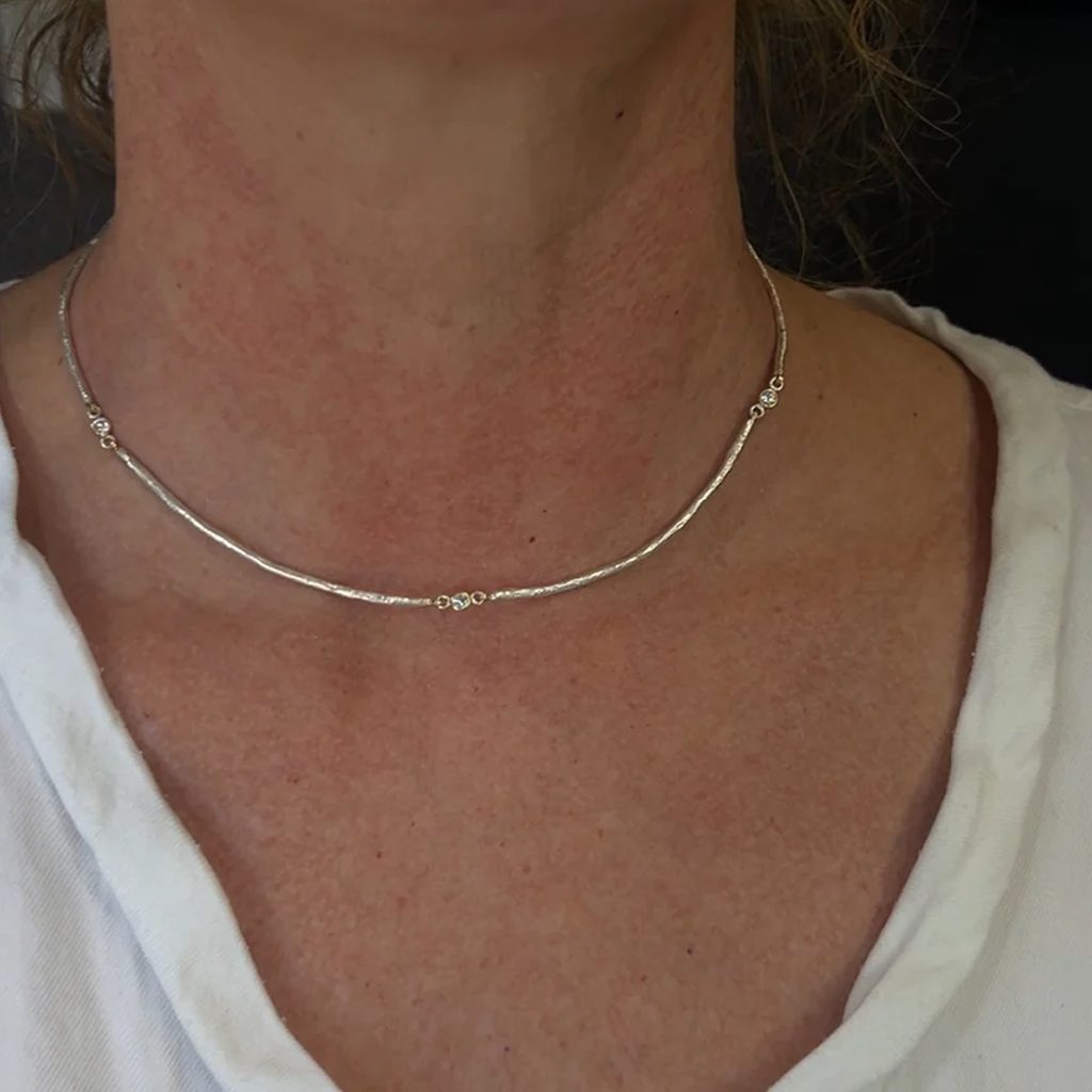 Close-up of a person wearing a gold necklace with Diamond stations wearing a white shirt.