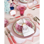 Pink scalloped-edge placemat with woven texture under floral patterned dinnerware on a table setting.