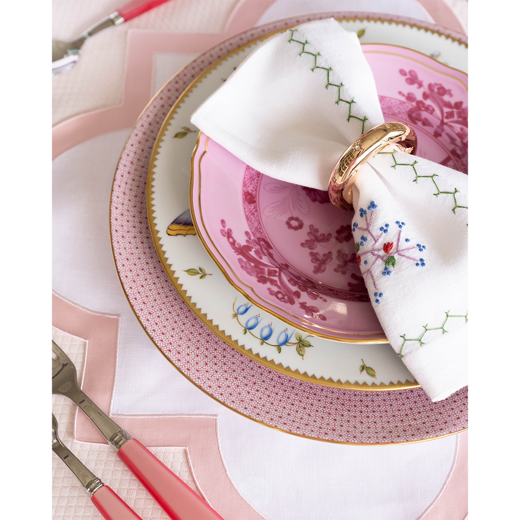 Pink scalloped placemat under decorative pink and white floral plates with a white napkin and gold napkin ring.