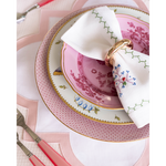 Pink scalloped placemat under decorative pink and white floral plates with a white napkin and gold napkin ring.