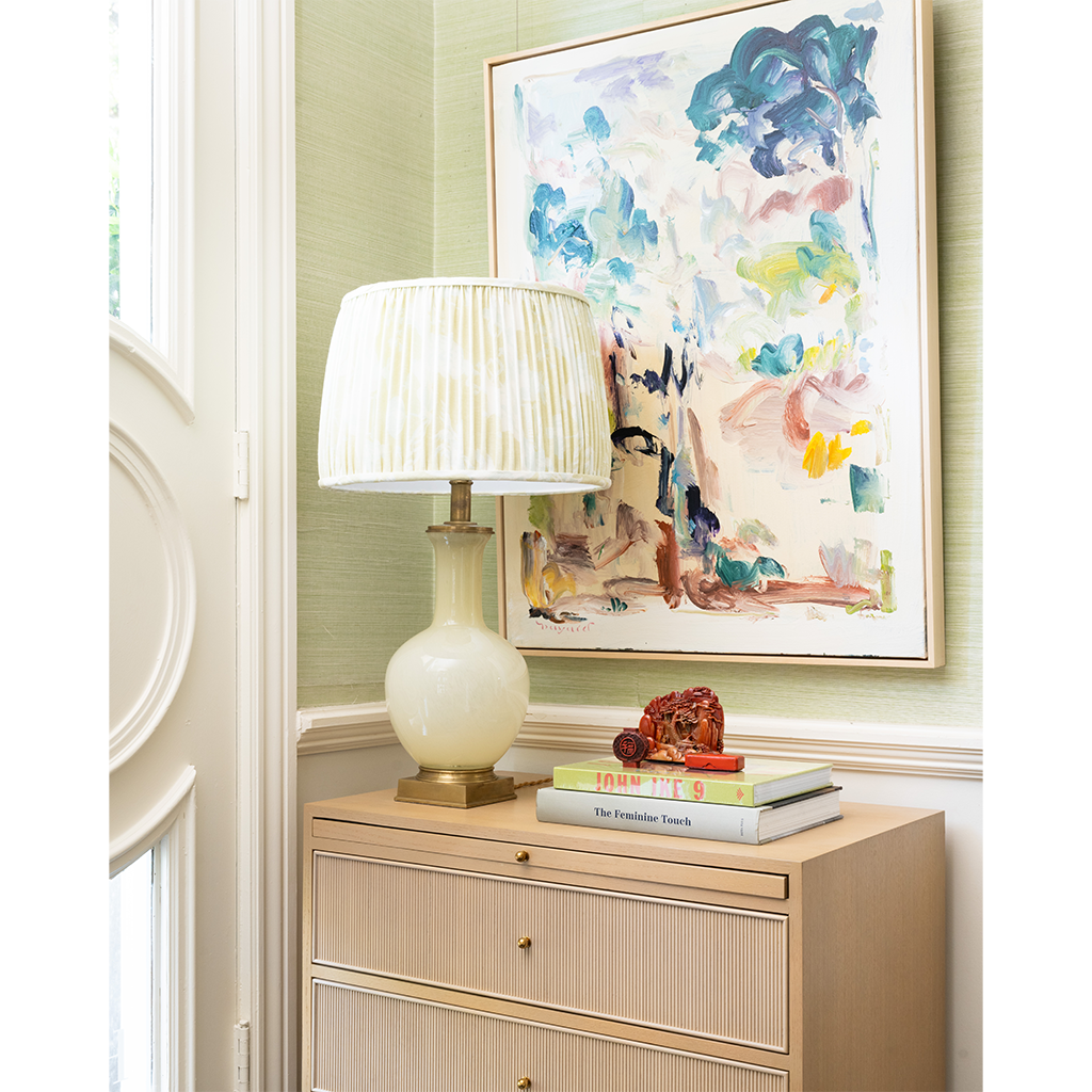 Decorative interior scene with a lamp, books, and artwork on a cabinet.