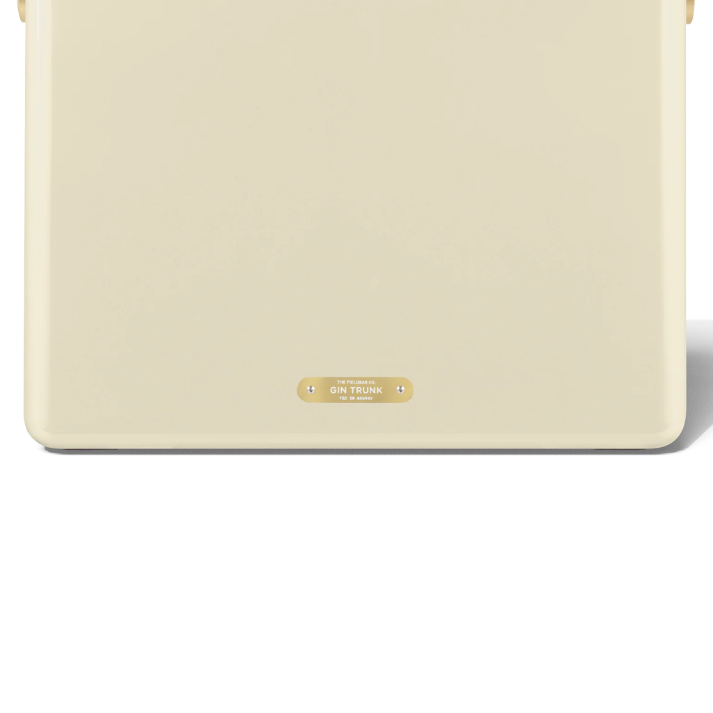 A close-up of the lower front of a cream FIELDBAR cooler highlights its smooth, rounded design and a small gold nameplate centered near the base. The gold plaque is engraved with the model name "Gin Trunk" and "Est. MMXXI," adding a refined finishing detail.