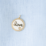 Round pendant with 'love' engraving on a light blue fabric background