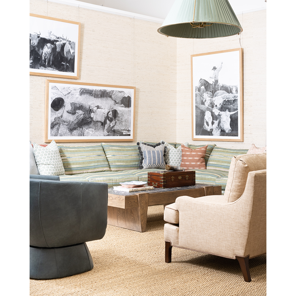 A styled living room featuring a striped green and beige sofa, a dark gray swivel chair, a beige armchair, a wooden coffee table, and three framed black-and-white art prints on a textured beige wall.