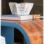 Decorative blue and white bowl on top of books with a wooden surface and blurred background