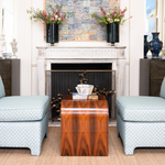 Living room with two patterned chairs and a wooden side table in front of a fireplace.