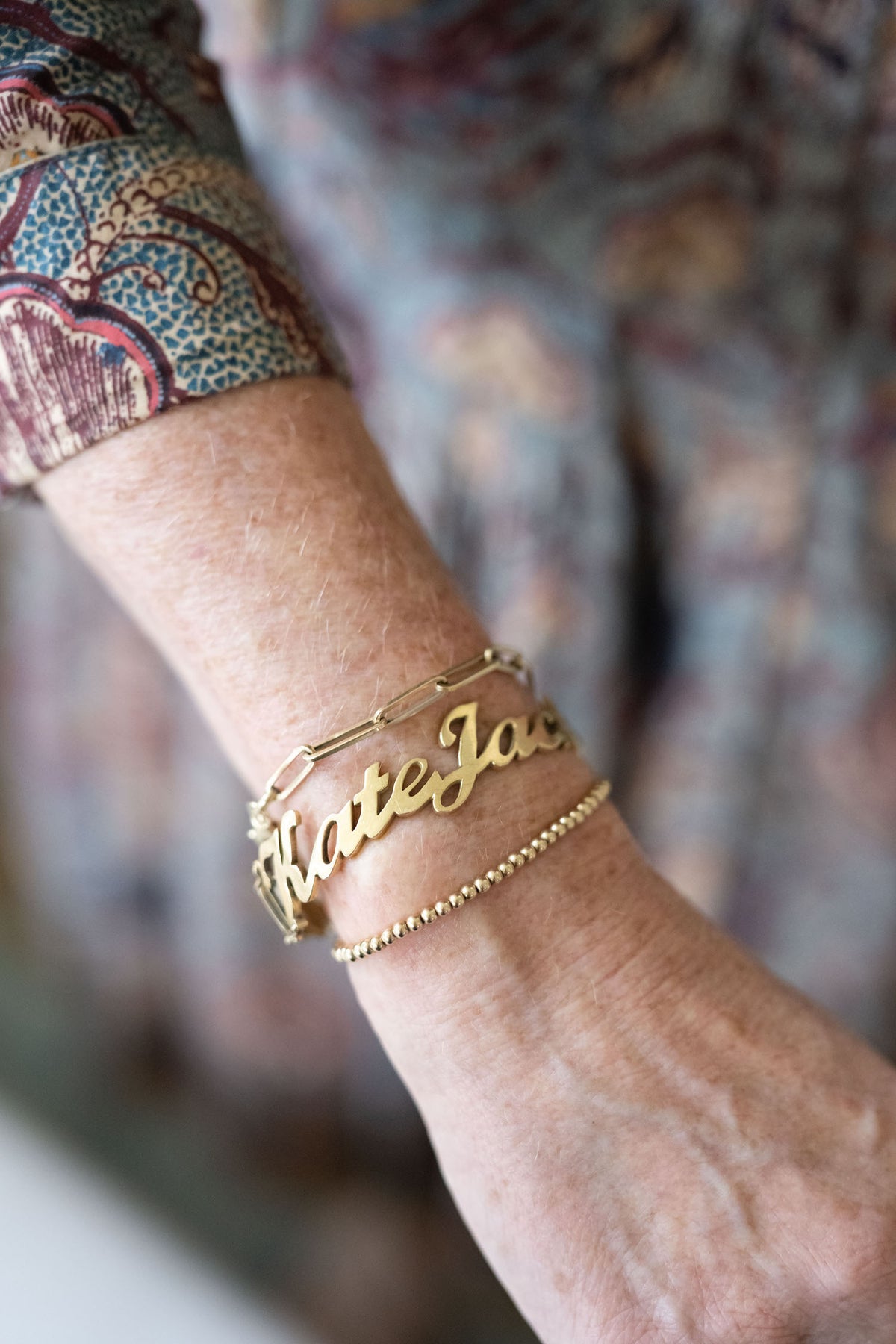 Gold name bracelet on model with additional bracelets