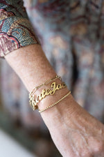 Gold name bracelet on model with additional bracelets
