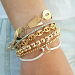 Stack of five gold bracelets featuring varied designs including linked chains, round beads, and a toggle clasp on a wrist.