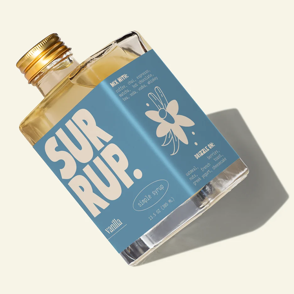 A bottle of SUR RUP. vanilla single syrup with a light blue label and gold cap, shown on a warm off-white background with a soft shadow.