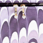 Heart-shaped diamond earrings on a purple and white patterned background