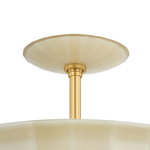 Close-up of a ceiling light fixture showing a brushed gold metal stem and canopy with a cream-colored glass shade against a white background.