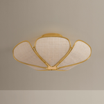 A modern semi-flush mount ceiling light fixture with a gold metal frame and textured beige fabric shades, shown against a neutral beige wall.