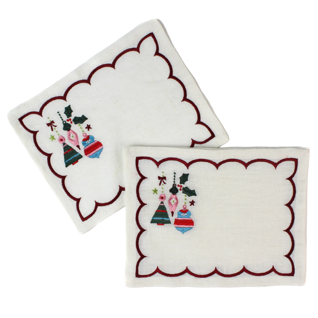 Two white embroidered square napkins with scalloped burgundy edges and a small Christmas ornament design in the lower left corner, shown on a white background.