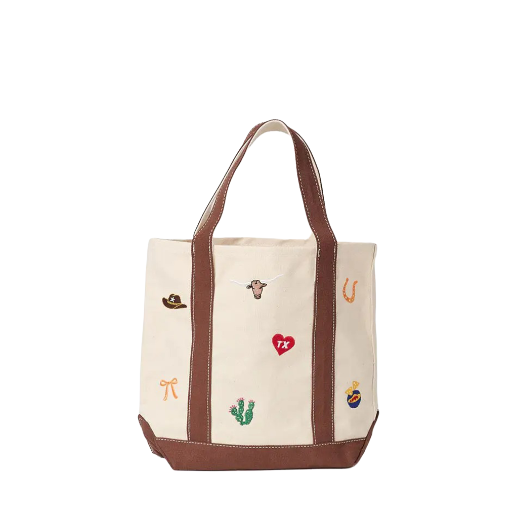 An off-white canvas tote bag with brown leather handles and base, decorated with small embroidered western-themed motifs including a cowboy hat, longhorn, horseshoe, cactus, and red heart.