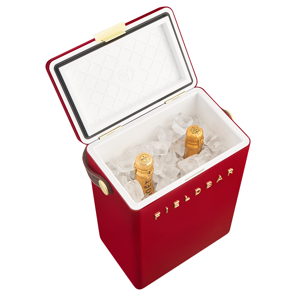 A red FIELDBAR cooler with its lid open, filled with ice and two champagne bottles, on a solid white background.