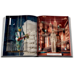 An open art book or magazine spread, showing two illustrated pages with surreal cityscapes, hanging mannequins, and decorative typography on a white background.