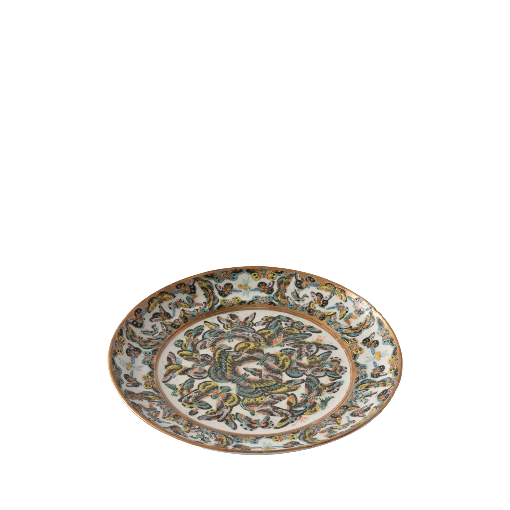 A decorative ceramic plate with a wide rim features an intricate hand-painted floral and vine pattern in shades of blue, green, brown, and gold on a white background. The center showcases a dense, symmetrical botanical design, framed by an ornate border with repeating leafy motifs.