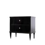 A three-quarter view of an antique ebonized two-drawer chest with a glossy black finish features clean, rectilinear lines, tapered legs, and ivory-colored shield-shaped keyhole escutcheons. The minimalist design and elegant proportions reflect the refined simplicity of the Biedermeier style.
