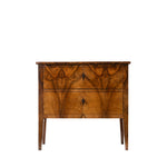 A vintage wooden nightstand featuring a rich, wavy grain pattern on its two drawers, with small dark metal key handles and tapered legs, shown against a plain white background.