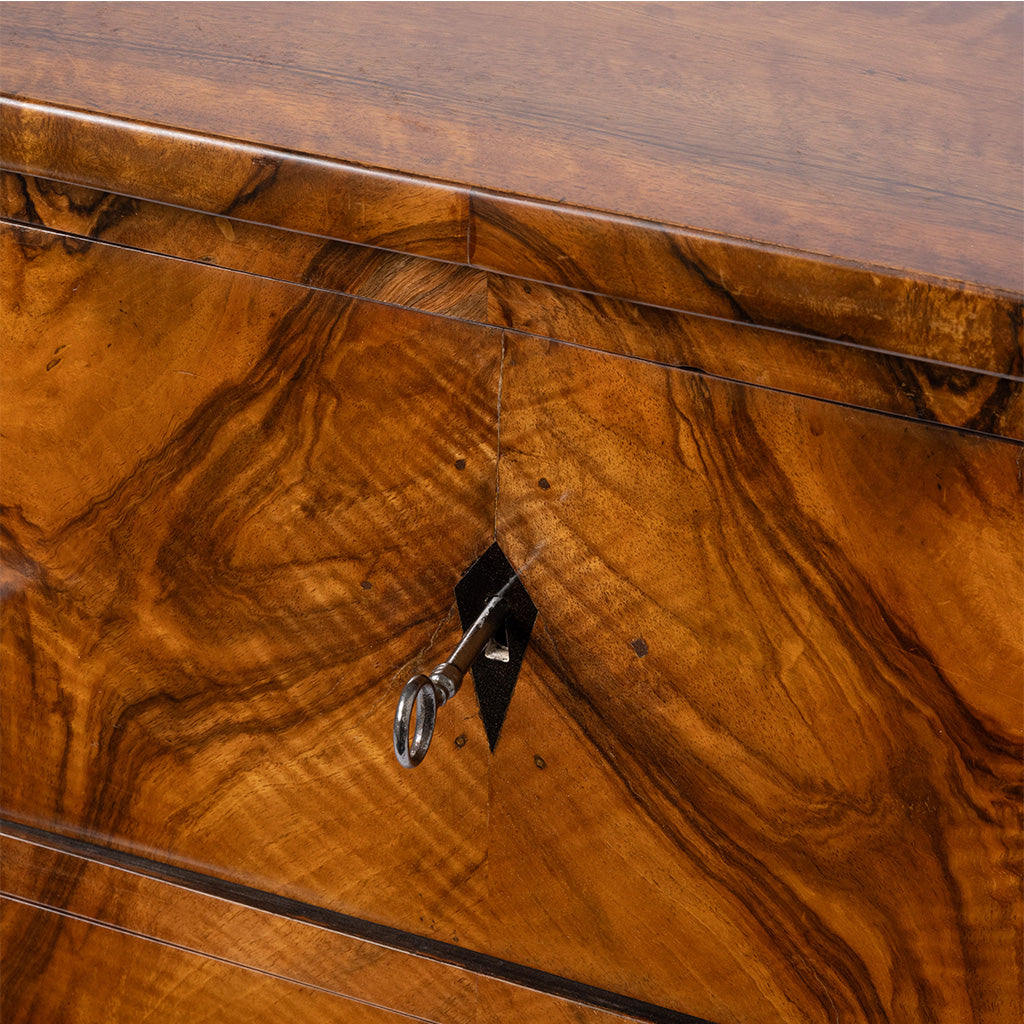 Close-up of a polished wooden side. table with a rich warm brown grain pattern, a central black diamond-shaped inlay holding a silver key, and thin dark inlaid lines.