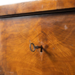 Close-up of a vintage wooden dresser drawer front with a warm honey-brown wood grain finish and a dark metal keyhole insert.