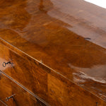 Close-up of a glossy medium-brown wooden chest with visible drawer fronts and small dark metal pulls.