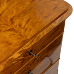 Close-up of a polished wood chest of drawers showing a rich flamed maple grain finish, drawer front, and metal drawer pulls against a white background.