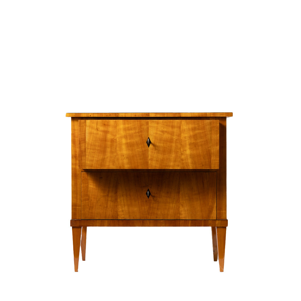 Front view of an antique Biedermeier two-drawer chest featuring a warm honey-colored wood veneer with beautifully matched figured grain across the drawer fronts. Simple diamond-shaped pulls, tapered legs, and clean, elegant lines reflect the refined craftsmanship of the Biedermeier style.