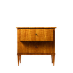 Front view of an antique Biedermeier two-drawer chest featuring a warm honey-colored wood veneer with beautifully matched figured grain across the drawer fronts. Simple diamond-shaped pulls, tapered legs, and clean, elegant lines reflect the refined craftsmanship of the Biedermeier style.