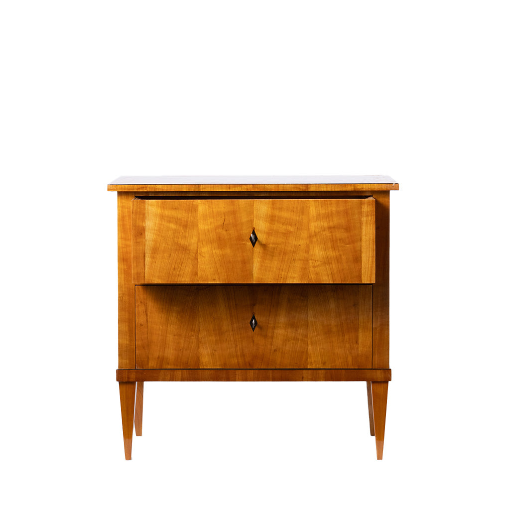 Front view of an antique Biedermeier two-drawer chest featuring a warm honey-colored wood veneer with beautifully matched figured grain across the drawer fronts. Simple diamond-shaped pulls, tapered legs, and clean, elegant lines reflect the refined craftsmanship of the Biedermeier style.