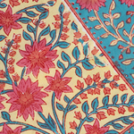 Beige tablecloth corner with pink floral print and blue leafy accents next to vibrant turquoise border with floral motifs.