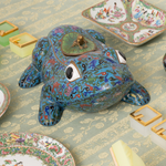 Decorative ceramic frog on a patterned surface with other decorative items.