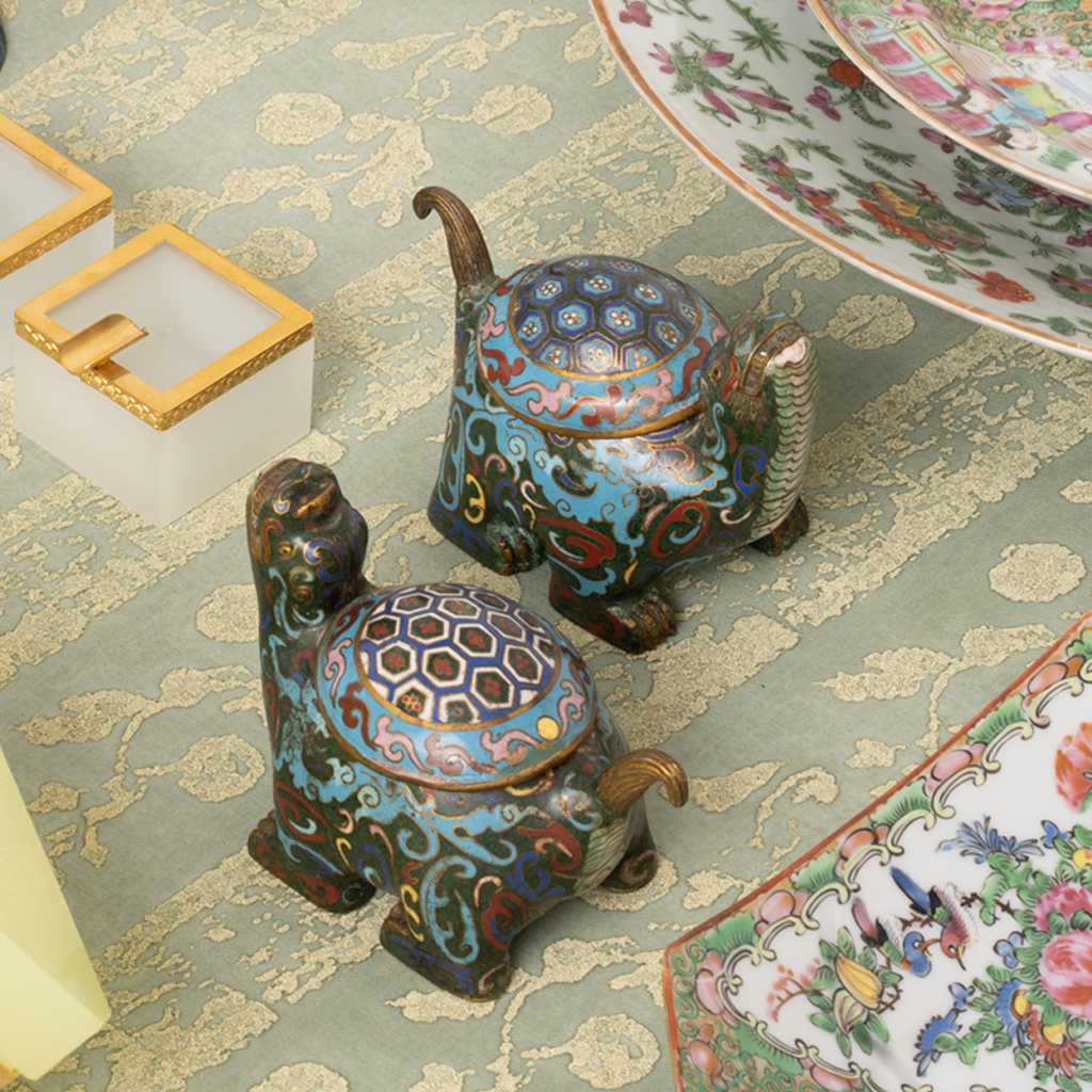 Decorative turtle-shaped cloisonne figurines on a patterned tablecloth