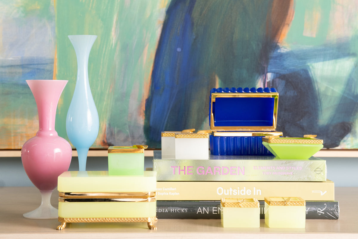 Colorful decorative items including vases and boxes on books with a blurred abstract painting in the background.