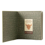 An open book or booklet with olive green pages covered in small white line drawings of various objects and symbols. A central cream label reads, "Every great story begins with a good drink.