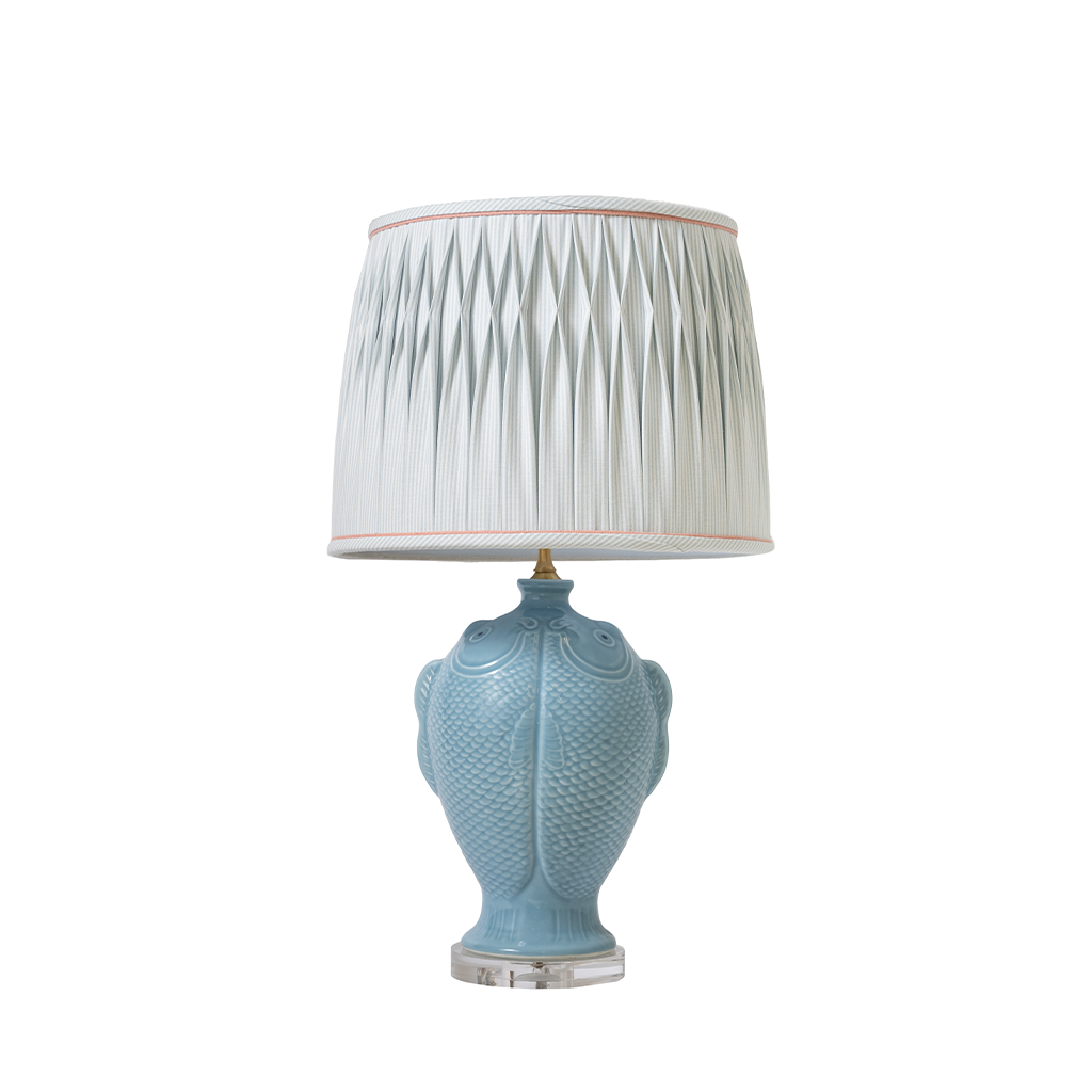 Blue ceramic table lamp with a white pleated shade on a white background