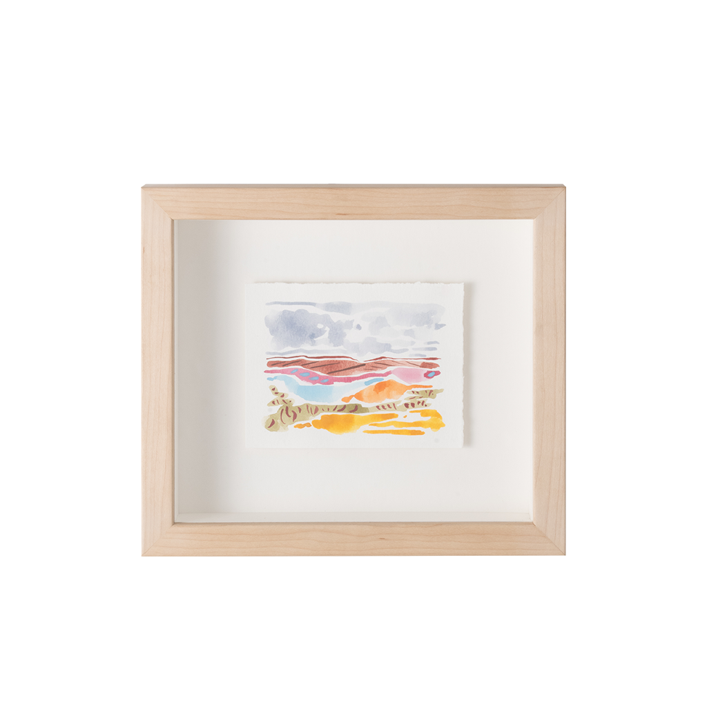 A small framed abstract watercolor painting with soft pastel bands in blue, pink, orange, and yellow, mounted in a light natural wood frame with a white mat against a white background.