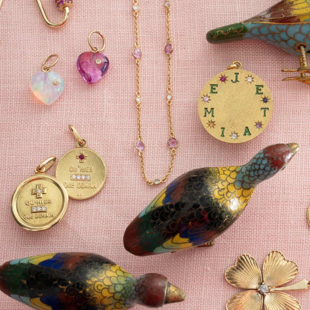 Collection of jewelry including necklaces, pendants, and a decorative bird on a pink background