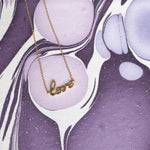 Gold bracelet with 'love' pendant on a purple abstract background