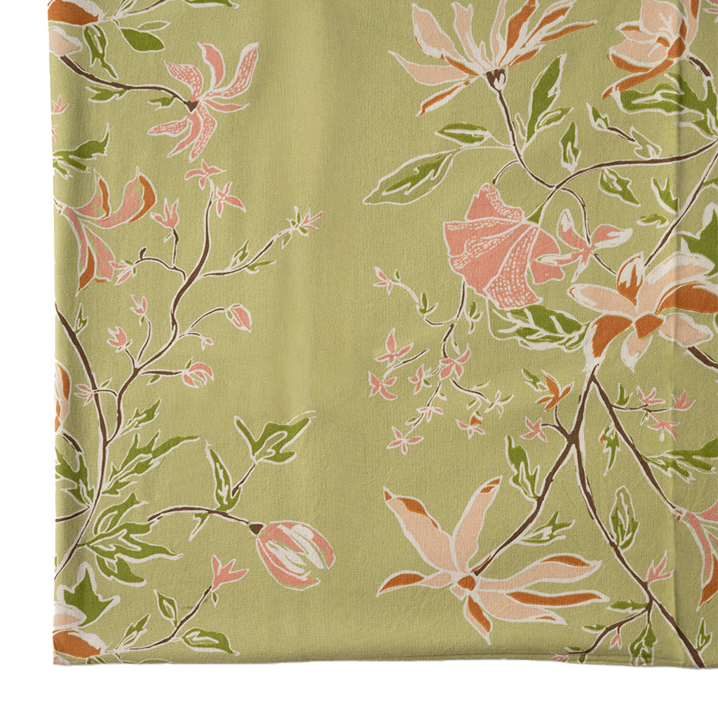 close up image of a green and orange botanical tablecloth on a white background