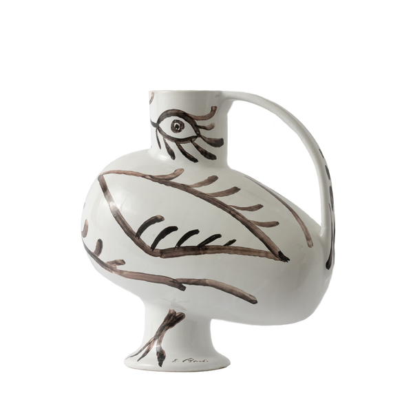 A white ceramic pitcher with a distinctive handle and footed base, decorated with brown hand-painted line art of a bird and eye motif, on a solid white background.